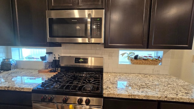 kitchen with light stone countertops, dark brown cabinetry, appliances with stainless steel finishes, and tasteful backsplash