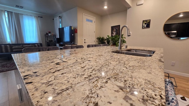 kitchen featuring light wood-style flooring, a sink, light stone counters, and visible vents