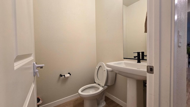 bathroom with baseboards, wood finished floors, and toilet