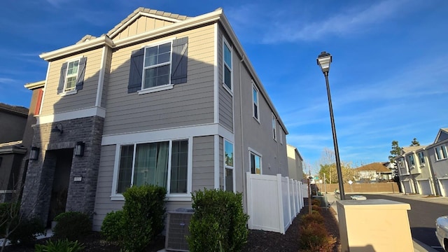 view of side of property featuring fence, brick siding, a tile roof, a residential view, and cooling unit