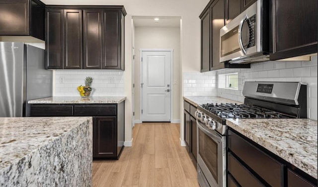 kitchen with light stone countertops, appliances with stainless steel finishes, light wood-type flooring, baseboards, and dark brown cabinets