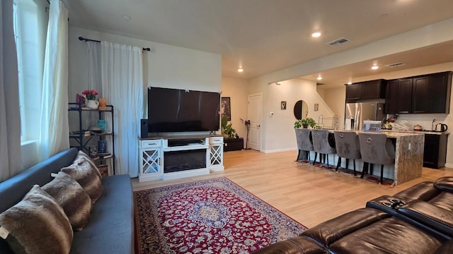 living room featuring baseboards, visible vents, recessed lighting, and light wood-type flooring