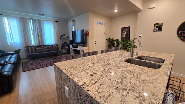 kitchen with a sink, light stone countertops, wood finished floors, open floor plan, and visible vents