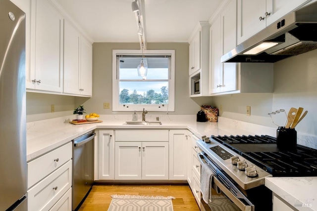 kitchen featuring white cabinetry, under cabinet range hood, a sink, light wood finished floors, and appliances with stainless steel finishes