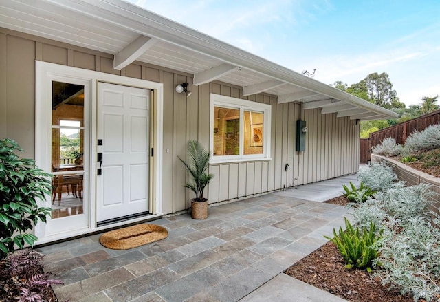 view of exterior entry with a patio area, fence, and board and batten siding