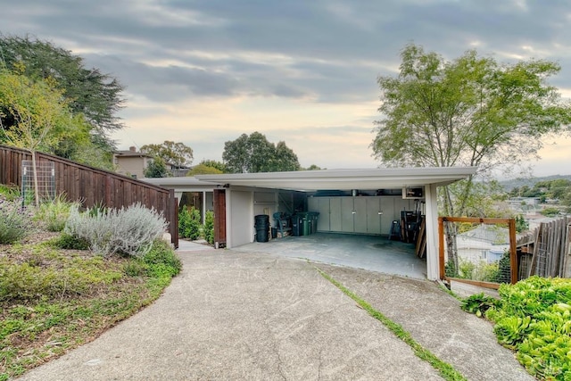 garage at dusk featuring fence, concrete driveway, and a carport