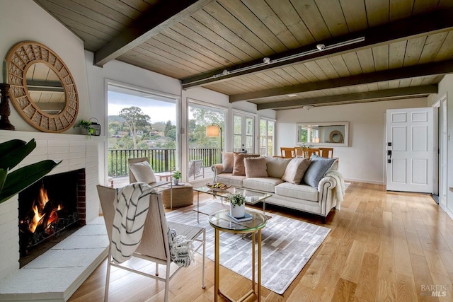 living area featuring wood ceiling, beamed ceiling, a brick fireplace, and light wood finished floors