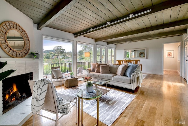 living room with wooden ceiling, a wealth of natural light, a brick fireplace, and light wood finished floors