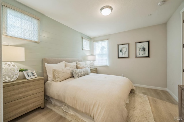 bedroom featuring wooden walls, baseboards, and light wood-type flooring
