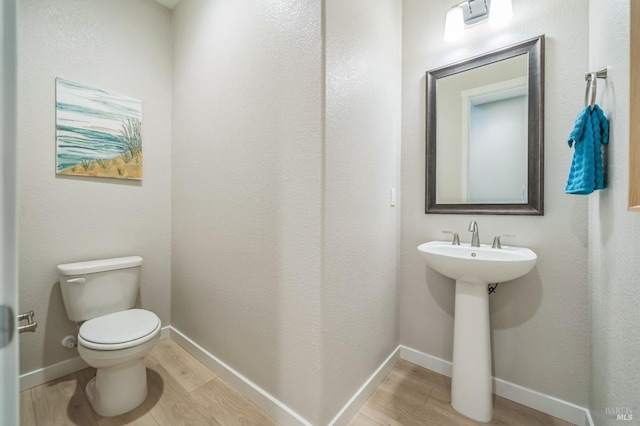 bathroom featuring baseboards, wood finished floors, and toilet
