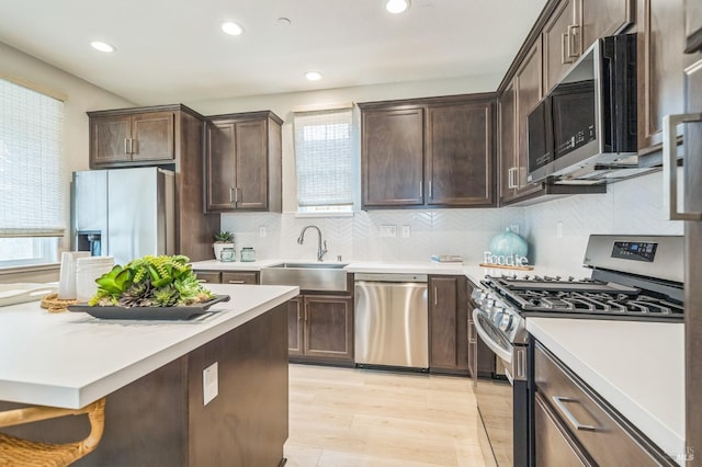 kitchen featuring dark brown cabinets, a sink, light countertops, stainless steel appliances, and a wealth of natural light