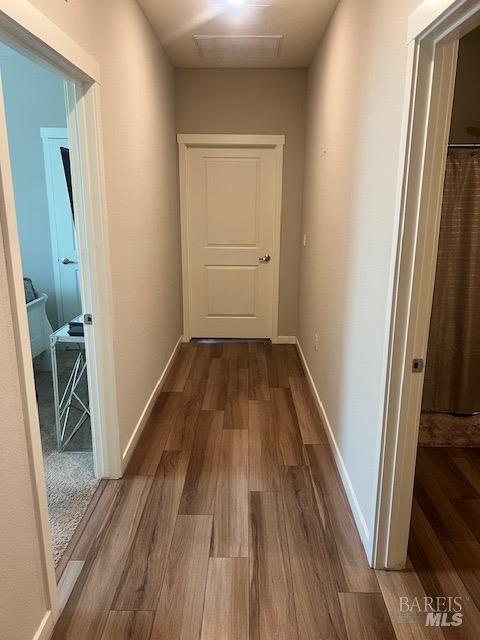 hallway featuring visible vents, baseboards, and wood finished floors