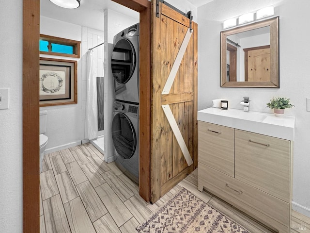 laundry area featuring laundry area, stacked washer and clothes dryer, baseboards, a barn door, and a sink
