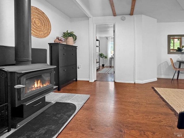 living room featuring baseboards, beamed ceiling, wood finished floors, and a wood stove