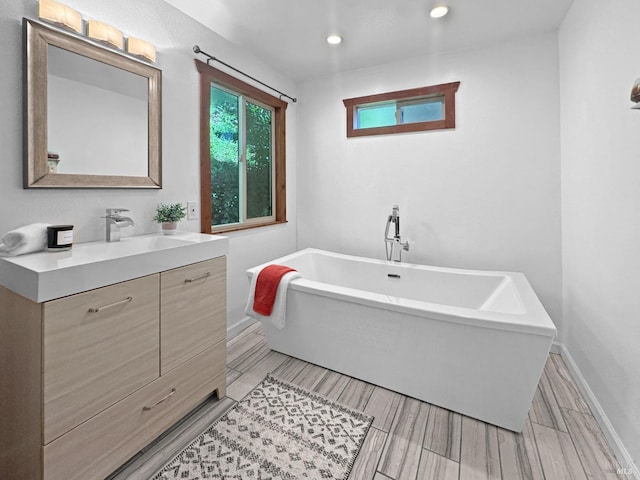 full bathroom with vanity, recessed lighting, baseboards, and a freestanding tub