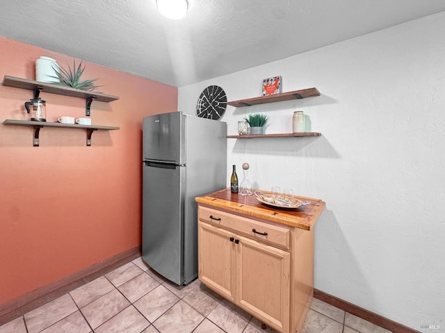 kitchen with freestanding refrigerator, open shelves, baseboards, butcher block countertops, and light tile patterned floors