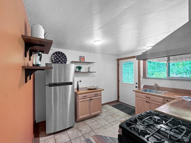 kitchen featuring black range with gas cooktop, open shelves, a sink, freestanding refrigerator, and light tile patterned flooring