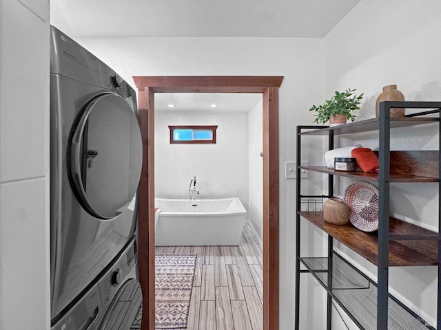 full bathroom featuring stacked washing maching and dryer, a freestanding tub, and wood finished floors