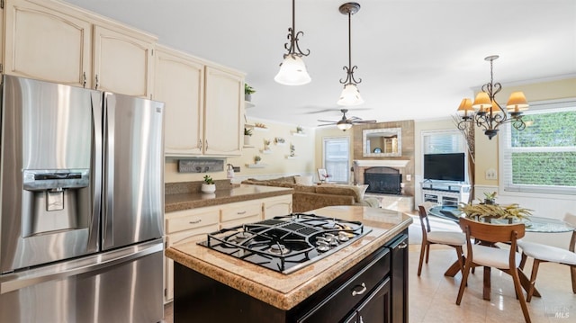 kitchen with ceiling fan with notable chandelier, cream cabinets, a fireplace, hanging light fixtures, and appliances with stainless steel finishes