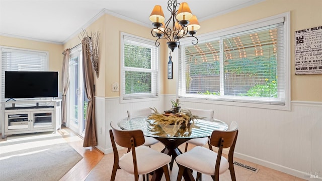 dining room featuring a wainscoted wall, crown molding, light wood-style flooring, and a notable chandelier