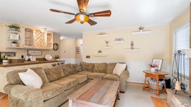 living area with a wainscoted wall, ceiling fan, and crown molding