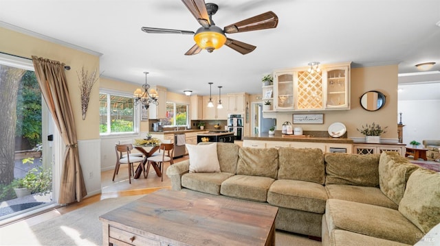living room featuring light wood-style flooring, crown molding, wainscoting, and ceiling fan with notable chandelier