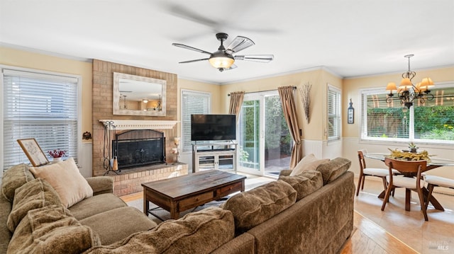 living room with light wood finished floors, a fireplace, ceiling fan with notable chandelier, and ornamental molding