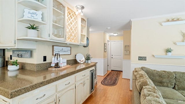 kitchen with a wainscoted wall, ornamental molding, open shelves, light wood finished floors, and glass insert cabinets