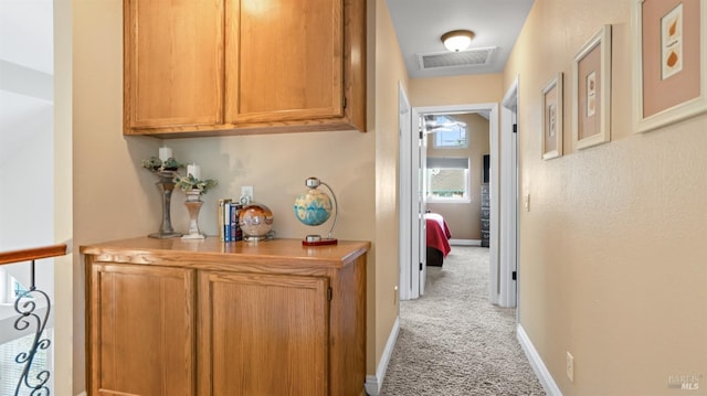 hallway featuring baseboards, light carpet, and visible vents