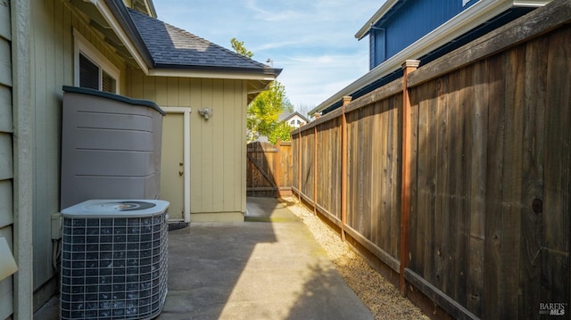 view of side of home featuring central AC unit, roof with shingles, fence, and a patio area