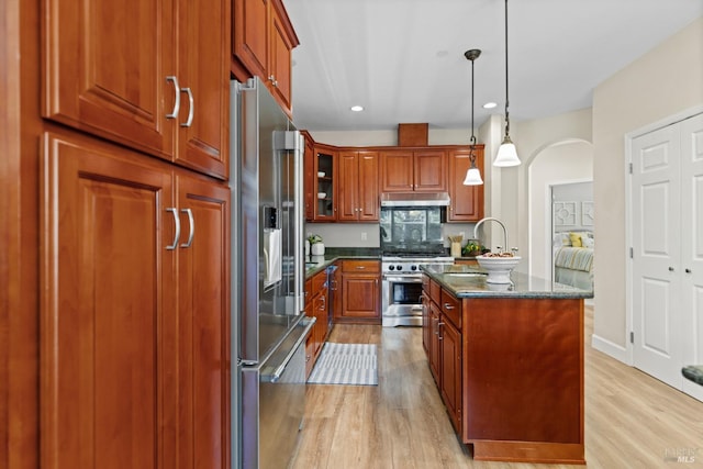 kitchen with arched walkways, a center island with sink, high end appliances, and light wood finished floors