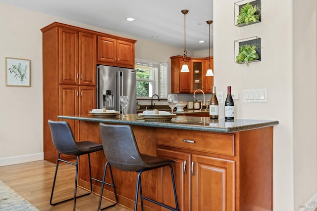 kitchen with a breakfast bar, brown cabinets, light wood-type flooring, high end refrigerator, and hanging light fixtures