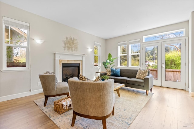 living area with a wealth of natural light, light wood-style flooring, french doors, and a tile fireplace