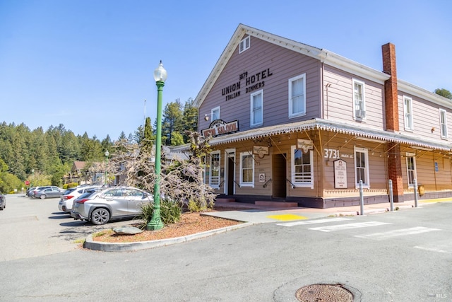 view of front of house featuring a porch, uncovered parking, and a chimney