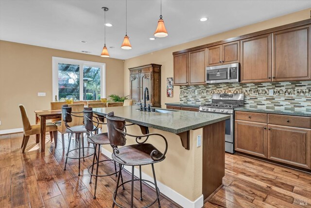 kitchen featuring decorative backsplash, stainless steel appliances, a sink, light wood-type flooring, and a kitchen breakfast bar