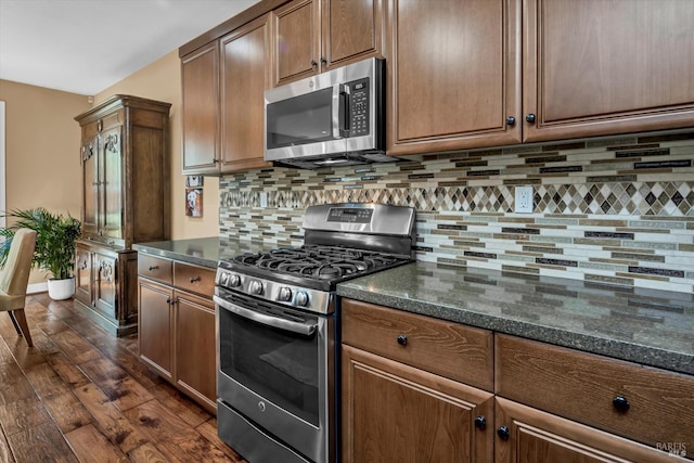 kitchen featuring decorative backsplash, baseboards, stainless steel appliances, dark stone counters, and dark wood-style floors