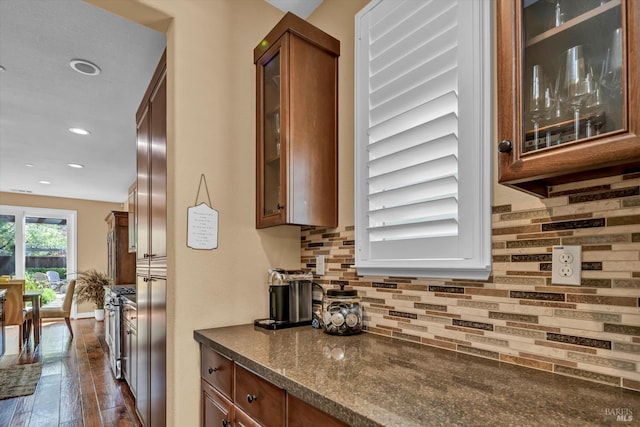 kitchen featuring stainless steel gas range, brown cabinets, tasteful backsplash, glass insert cabinets, and dark wood-style floors