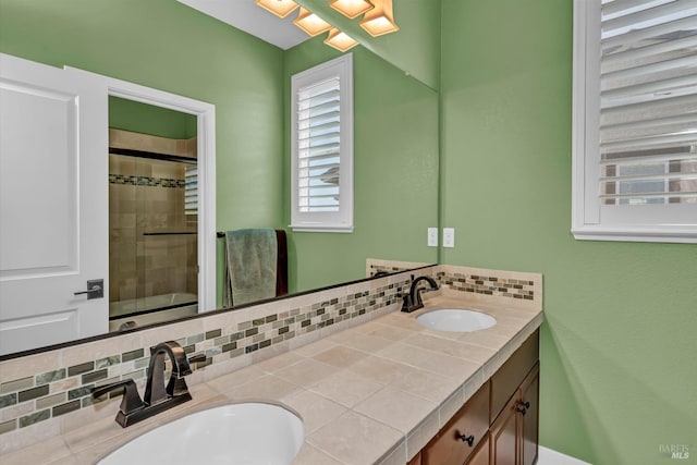 bathroom with decorative backsplash, double vanity, a sink, and a shower with door