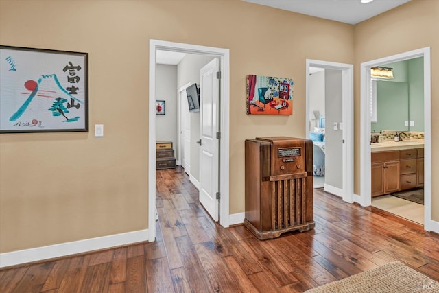 hallway featuring dark wood-style flooring, a sink, and baseboards