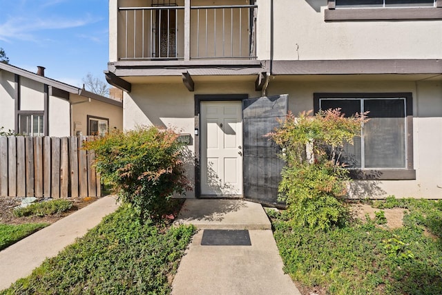 property entrance featuring stucco siding, fence, and a balcony
