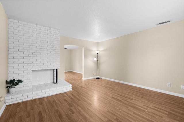 unfurnished living room with arched walkways, baseboards, visible vents, and wood finished floors