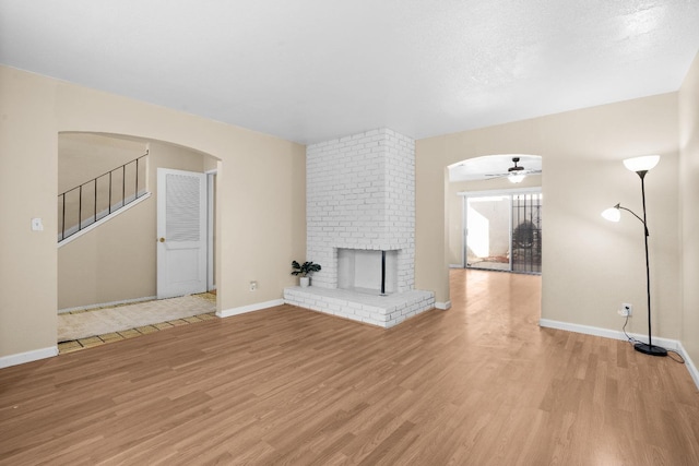 unfurnished living room with a ceiling fan, arched walkways, baseboards, and light wood-type flooring