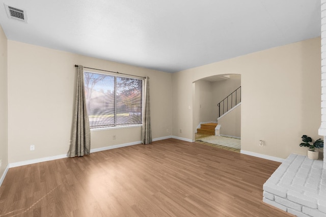 unfurnished living room with visible vents, arched walkways, light wood-style floors, and baseboards
