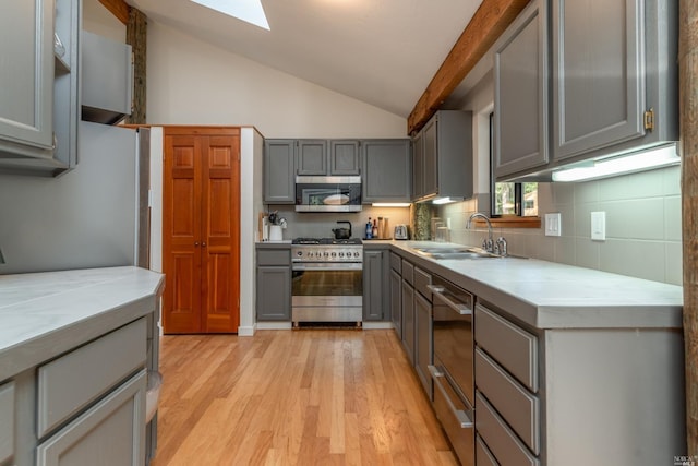 kitchen featuring light countertops, lofted ceiling with skylight, gray cabinets, a sink, and appliances with stainless steel finishes