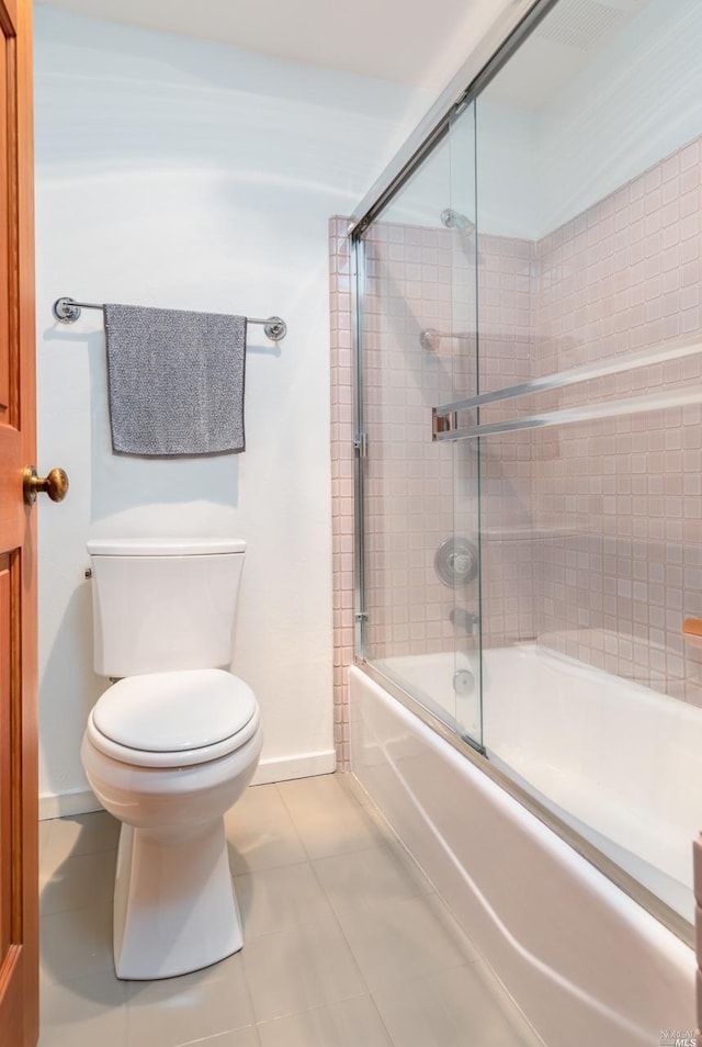 bathroom featuring baseboards, toilet, tile patterned flooring, and bath / shower combo with glass door