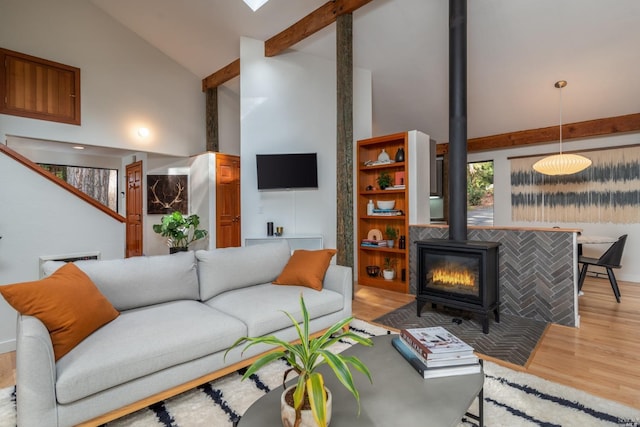 living room with wood finished floors, high vaulted ceiling, beam ceiling, and a wood stove
