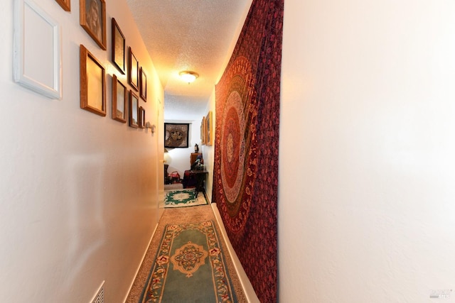 hallway with baseboards, carpet floors, a textured ceiling, and visible vents
