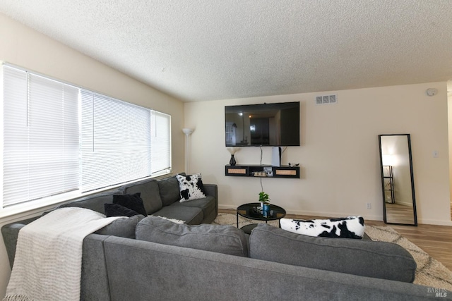 living area featuring baseboards, a textured ceiling, visible vents, and wood finished floors