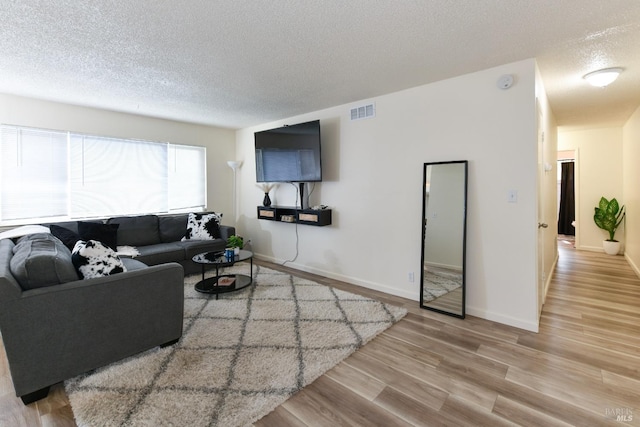 living area with baseboards, visible vents, wood finished floors, and a textured ceiling
