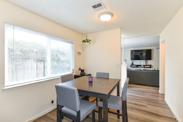 dining area featuring light wood finished floors, baseboards, visible vents, and a textured ceiling